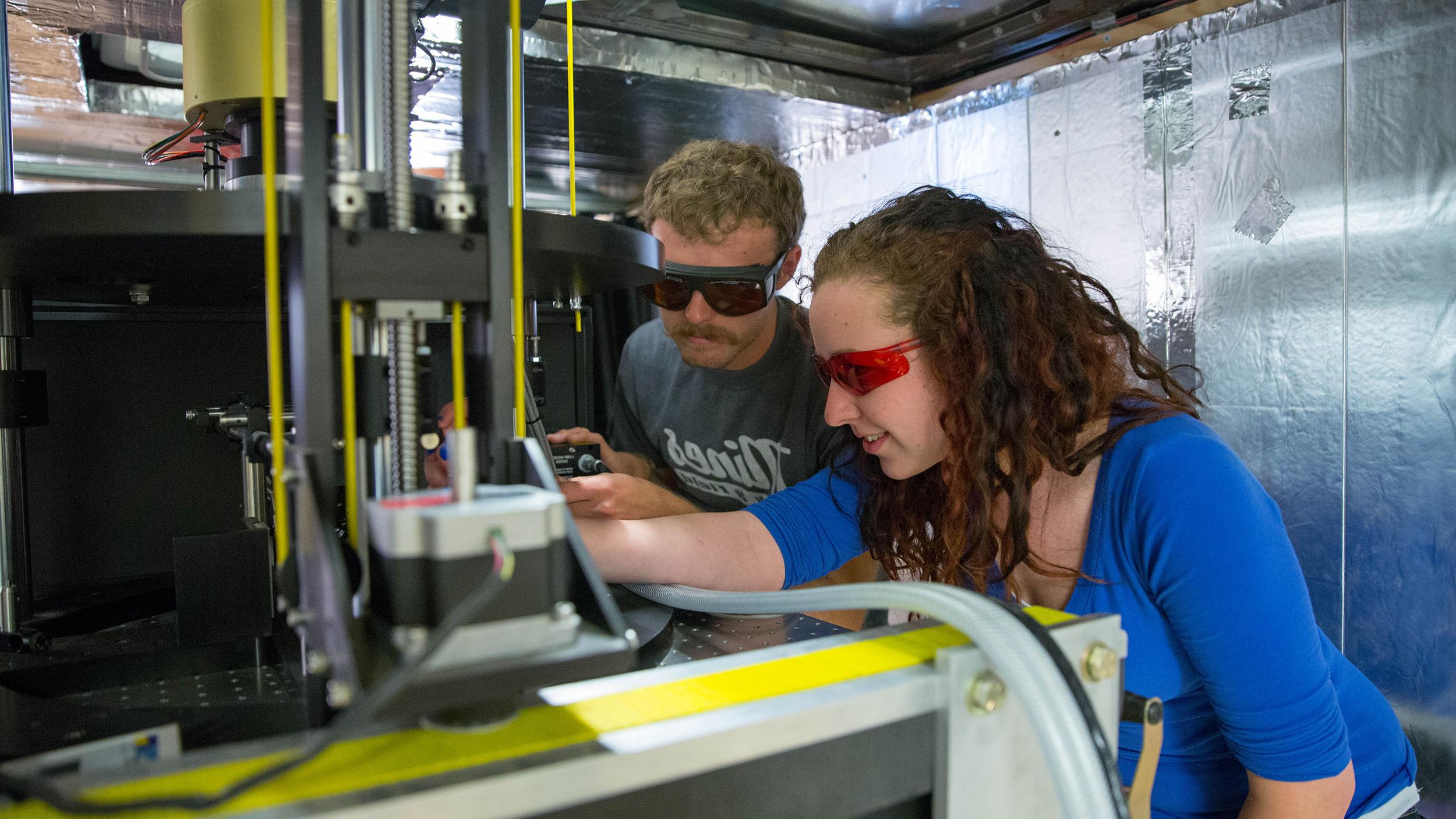 Two students focus on machinery in a lab